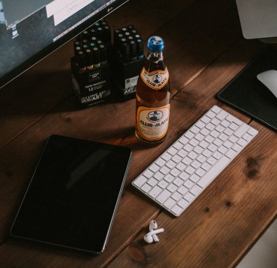 Holzschreibtisch und Arbeitsplatz mit einer Tastatur, Maus, Kopfhörer, Monitor und Erfrischungsgetränk